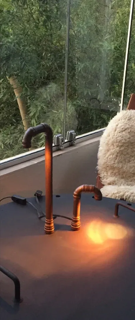 Duas luminárias de cobre em uso sobre mesa escura, diante de uma janela